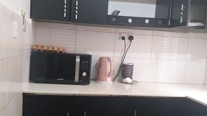 Een keuken met zwarte kastjes, een magnetron, een roze koffiezetapparaat en een voorraadbus.
