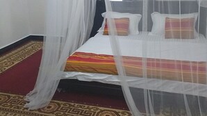 Een bed met een witte hemel en een beddekleed met een patroon, een rood en gouden vloerkleed en een vloermat met een ontwerp.