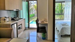 A modern hotel room with a kitchenette, a dining area, a bed, and a balcony with a pool view. - Arcadia Family Suite (Pattaya)
