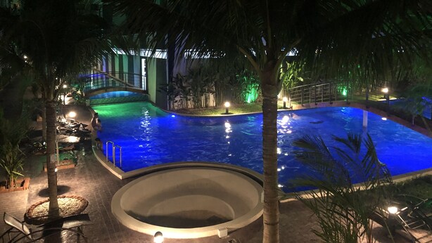 A nighttime swimming pool area with a circular hot tub, palm trees, and a building in the background. - Arcadia Family Suite (Pattaya)
