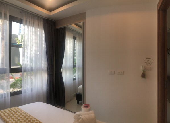 A hotel room with a bed, a bathroom mirror, and a window with sheer curtains. - Arcadia Family Suite (Pattaya)