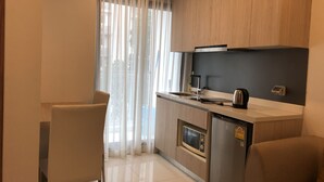 A modern kitchen with wooden cabinets, a stainless steel refrigerator, a microwave, and a kettle. - Arcadia Family Suite (Pattaya)