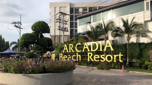 A sign for Arcadia Beach Resort with a paved area, palm trees, and a building in the background. - Arcadia Family Suite (Pattaya)