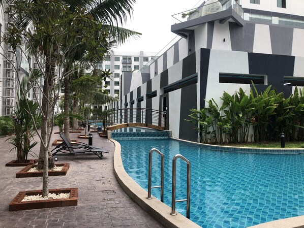 A modern pool area with a clear blue pool, surrounded by palm trees and a building with a geometric facade.
