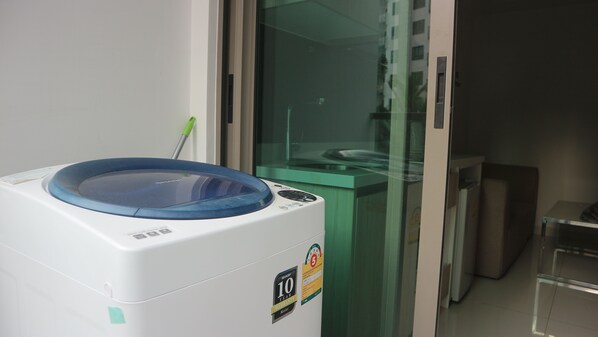 A front-loading washing machine with a blue lid, a Sharp 10-year warranty sticker, and a green cleaning tool nearby.