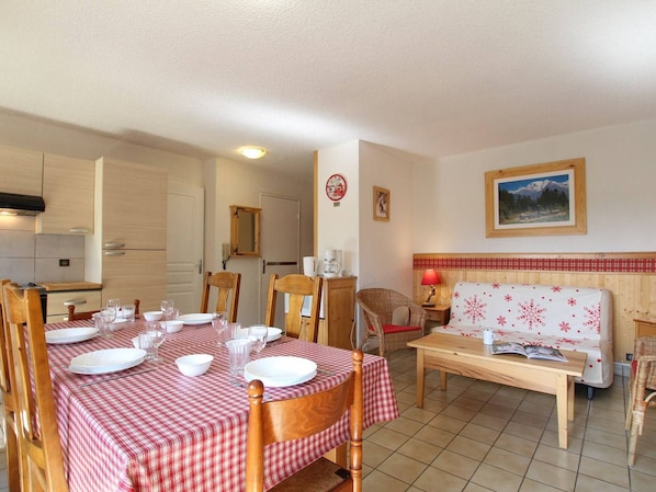 A dining area with a checkered tablecloth, wooden chairs, and a wooden table. There is a sofa with a red and white checkered cover, a wooden cabinet, and a framed picture on the wall.