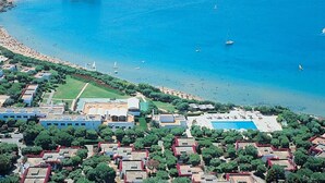 An aerial view of a coastal area with a large pool, a beach, and a small island with ruins.