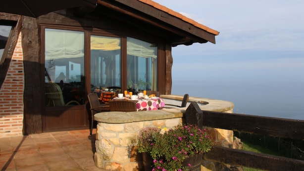 Um pátio de pedra com uma mesa posta para o café da manhã, com vista para um corpo d'água.