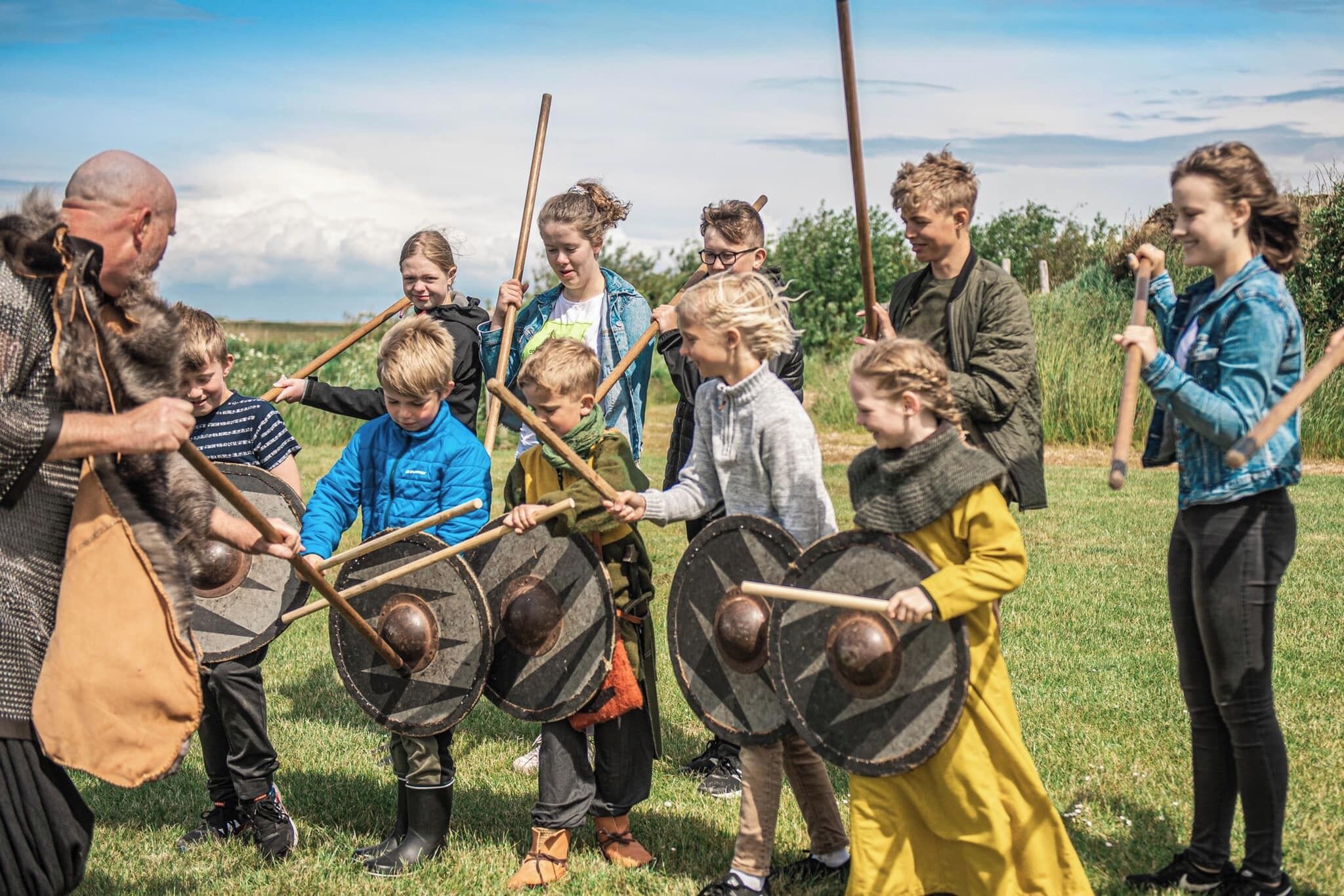 A group of people in a grassy outdoor area, some holding shields and others in casual clothing.