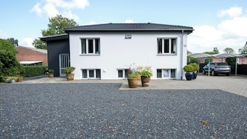 Une maison moderne à deux étages, avec une allée en gravier, des plantes en pot et une voiture garée.