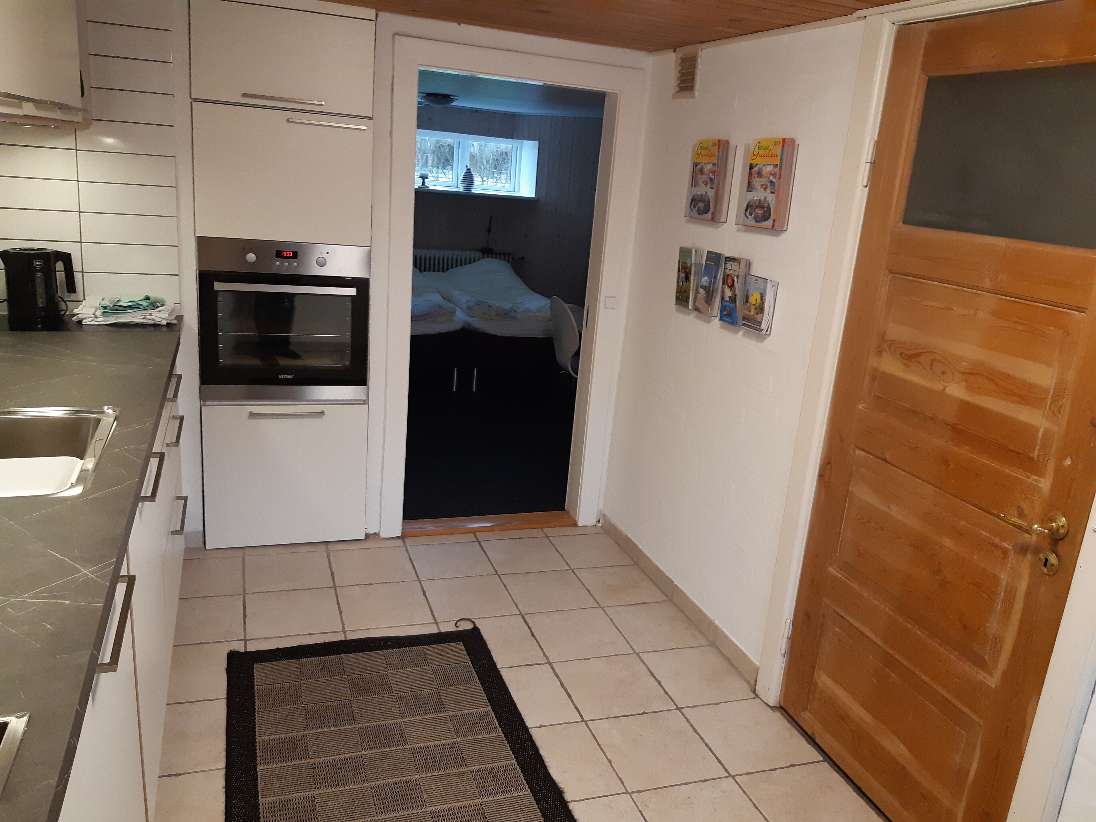 A compact kitchen with a built-in oven, a small sink, and a window with blinds.