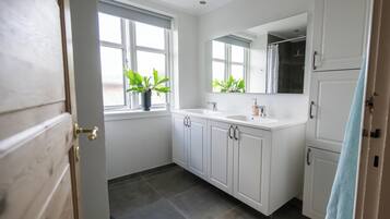 A modern bathroom with white cabinetry, a large mirror, and a potted plant by the window.