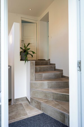 A staircase with beige tiles leading to a door, a potted plant on the wall, and a dark carpet at the bottom. - Sdr. Omme Bed & Breakfast (Sonder Omme)