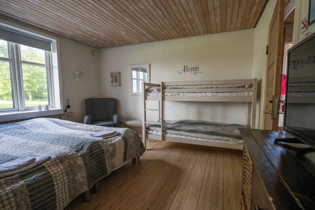 Ein Zimmer mit zwei Etagenbetten, einem Sessel, einem Schreibtisch und einem Fernseher.
