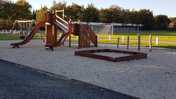 Ein Spielplatz mit Rutsche und Klettergerüsten, umgeben von Sand und einem befestigten Weg.