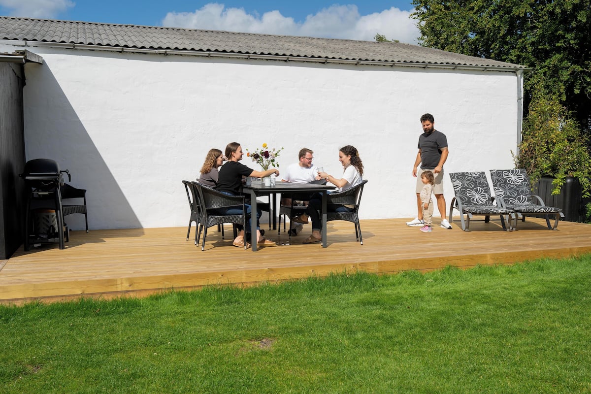 Eine Terrasse mit Tisch und Stühlen, einem Grill und einer weißen Wand im Hintergrund.
