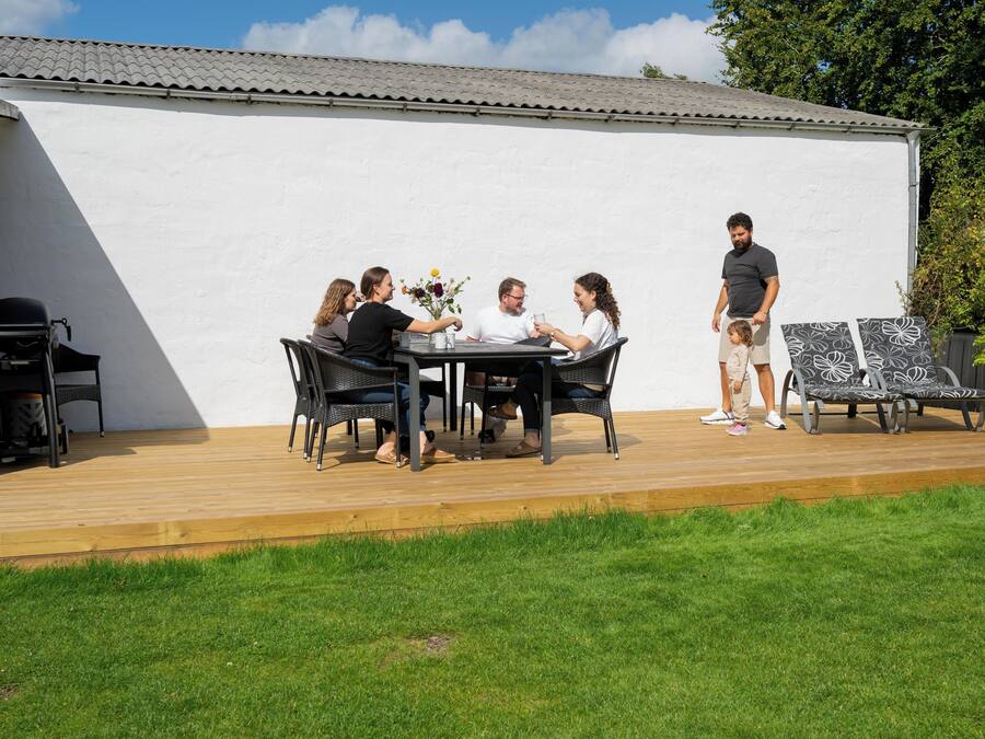 Un patio con mesa y sillas, una parrilla y un muro blanco al fondo.