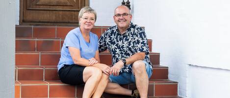 Two people sitting on a staircase with a wooden door and wall-mounted plaques in the background.