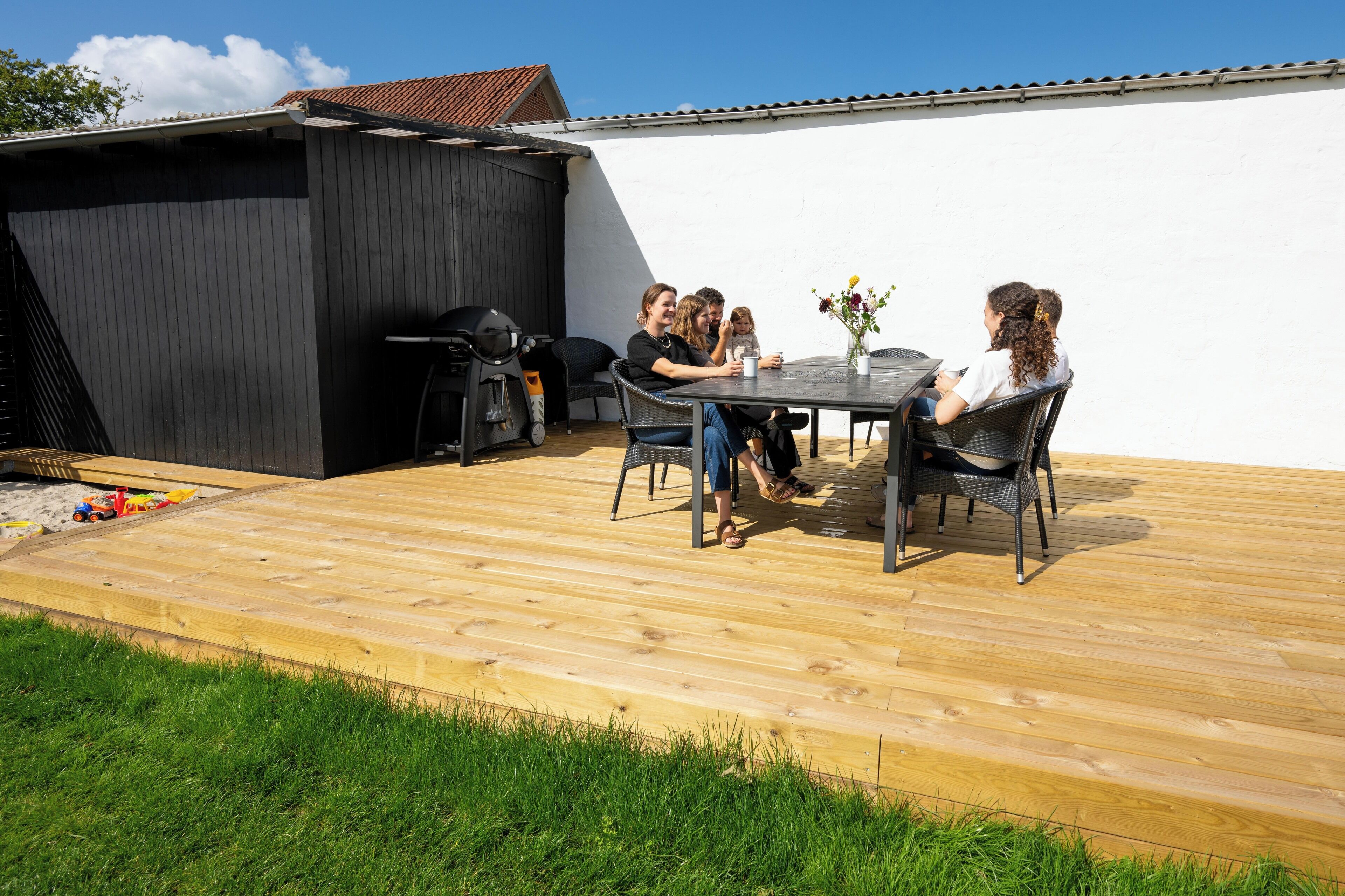 A patio with a table and chairs, a grill, and a small shed.