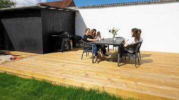 A patio with a table and chairs, a grill, and a small shed.