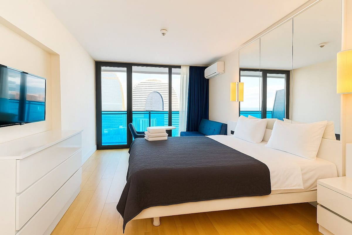 Een moderne hotelkamer met een groot bed, een flatscreen televisie, een balkon met uitzicht op de stad en een grote spiegel.