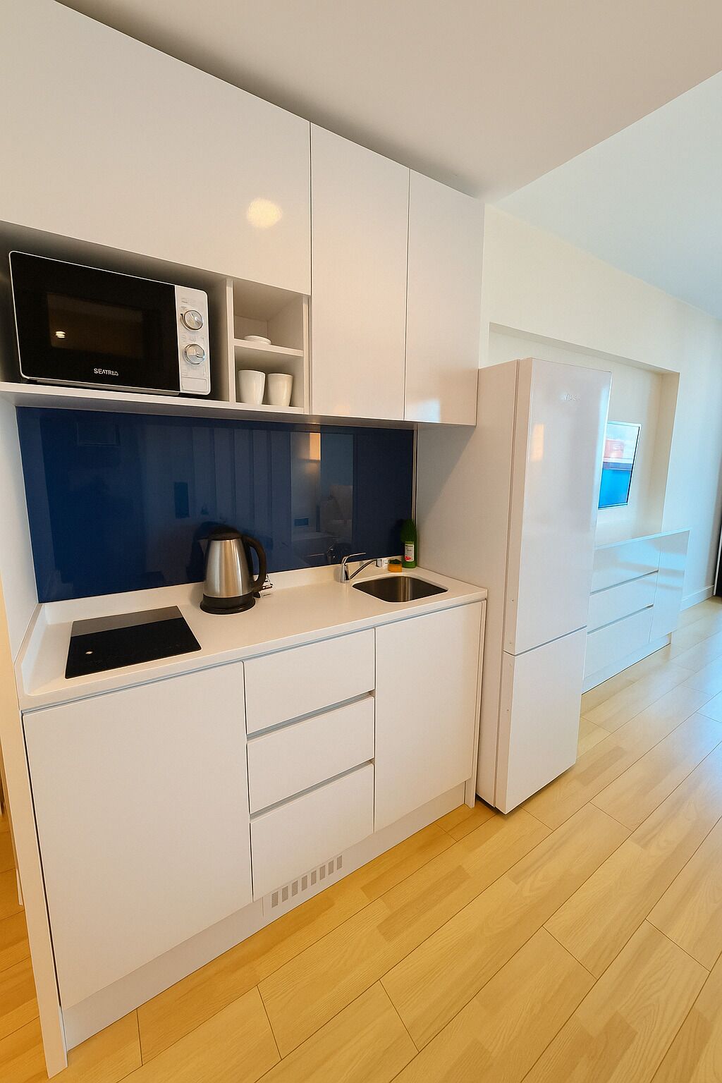 Une cuisine moderne dotée de meubles blancs, d’un four à micro-ondes, d’une bouilloire et d’un réfrigérateur.