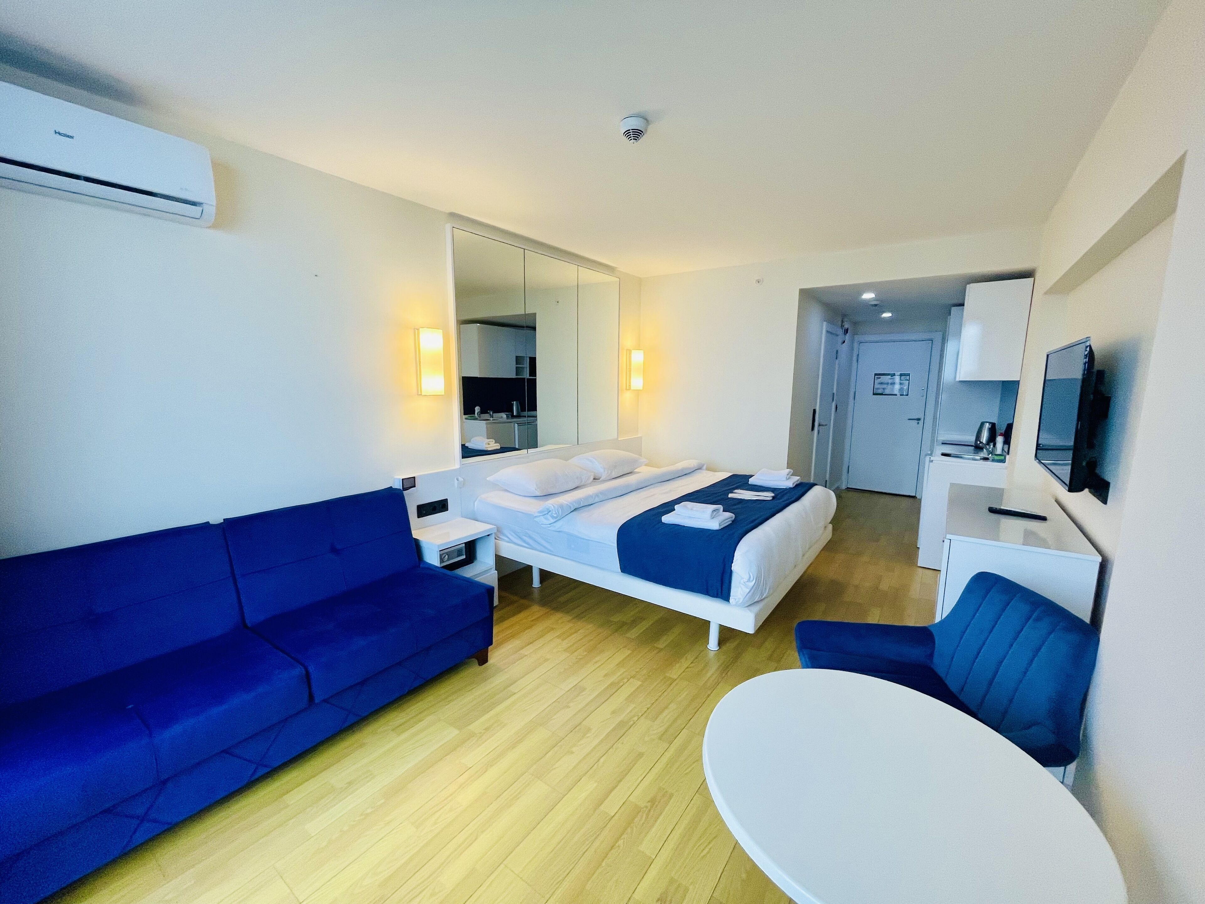A modern hotel room with a bed, a blue sofa, a small table, and a TV.