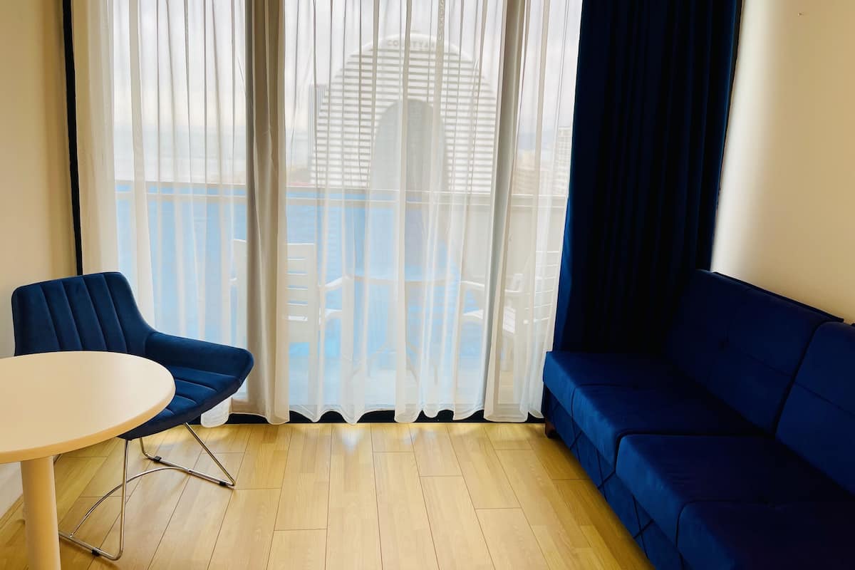Een kamer met een blauwe bank, een ronde tafel en dunne gordijnen.