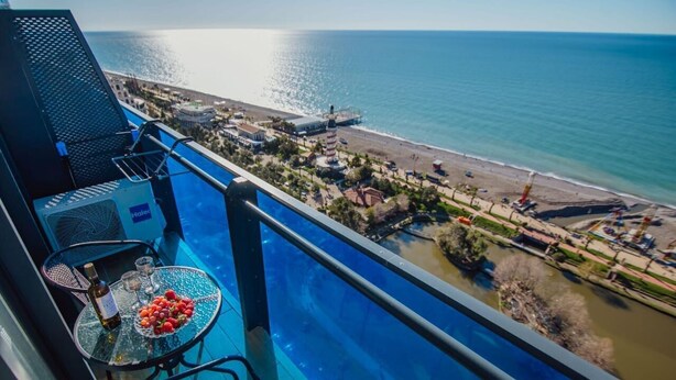 Un balcón con piscina, una mesa con una botella y vasos, y un cuenco de fruta.