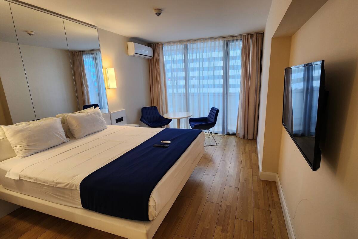 Hotelkamer met een groot bed, een televisie, een bureau met stoel en een raam met gordijnen.