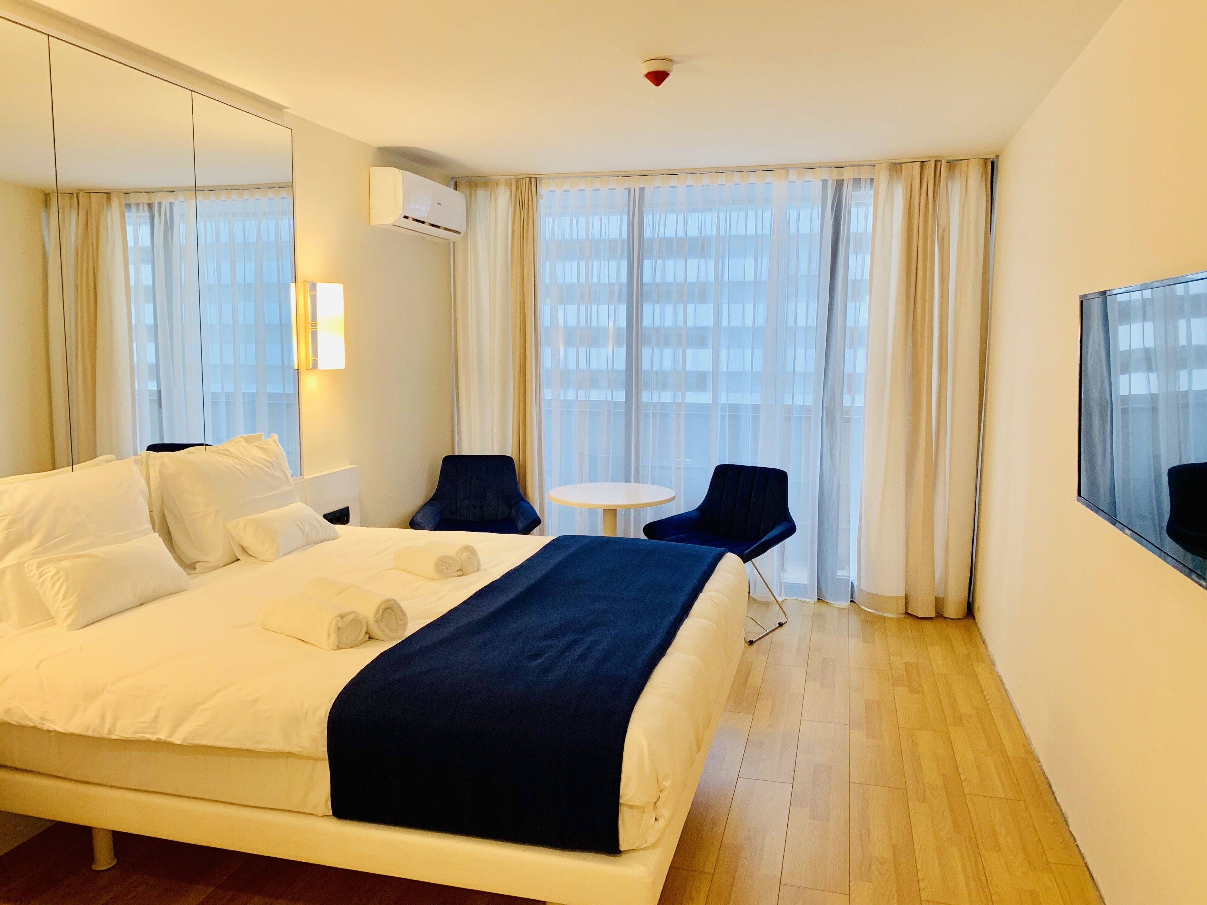 Een hotelkamer met een groot bed, een klein rond tafeltje, twee stoelen en een grote spiegel.