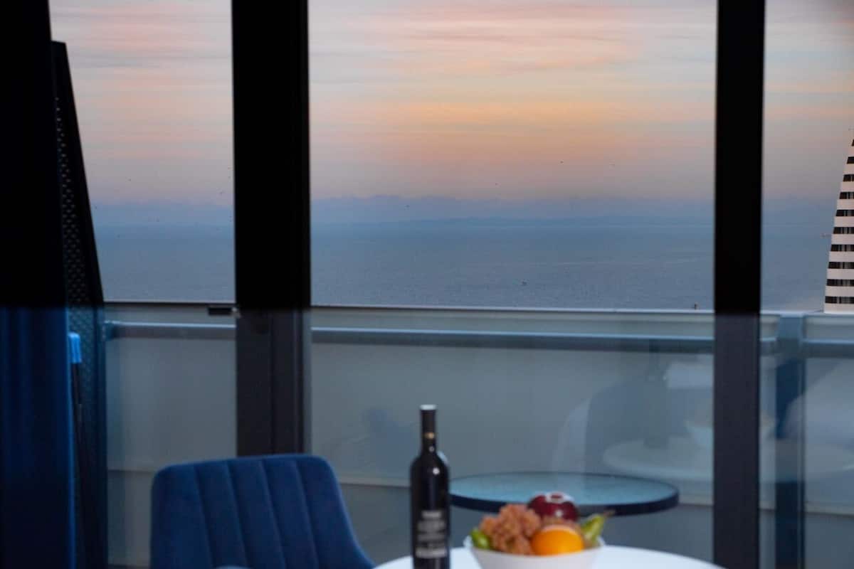 Een balkon met een tafel, een stoel, een fles en een schaal fruit.