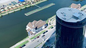 Vista aérea de una zona costera con un puerto deportivo, una playa y un edificio moderno con techo curvo.