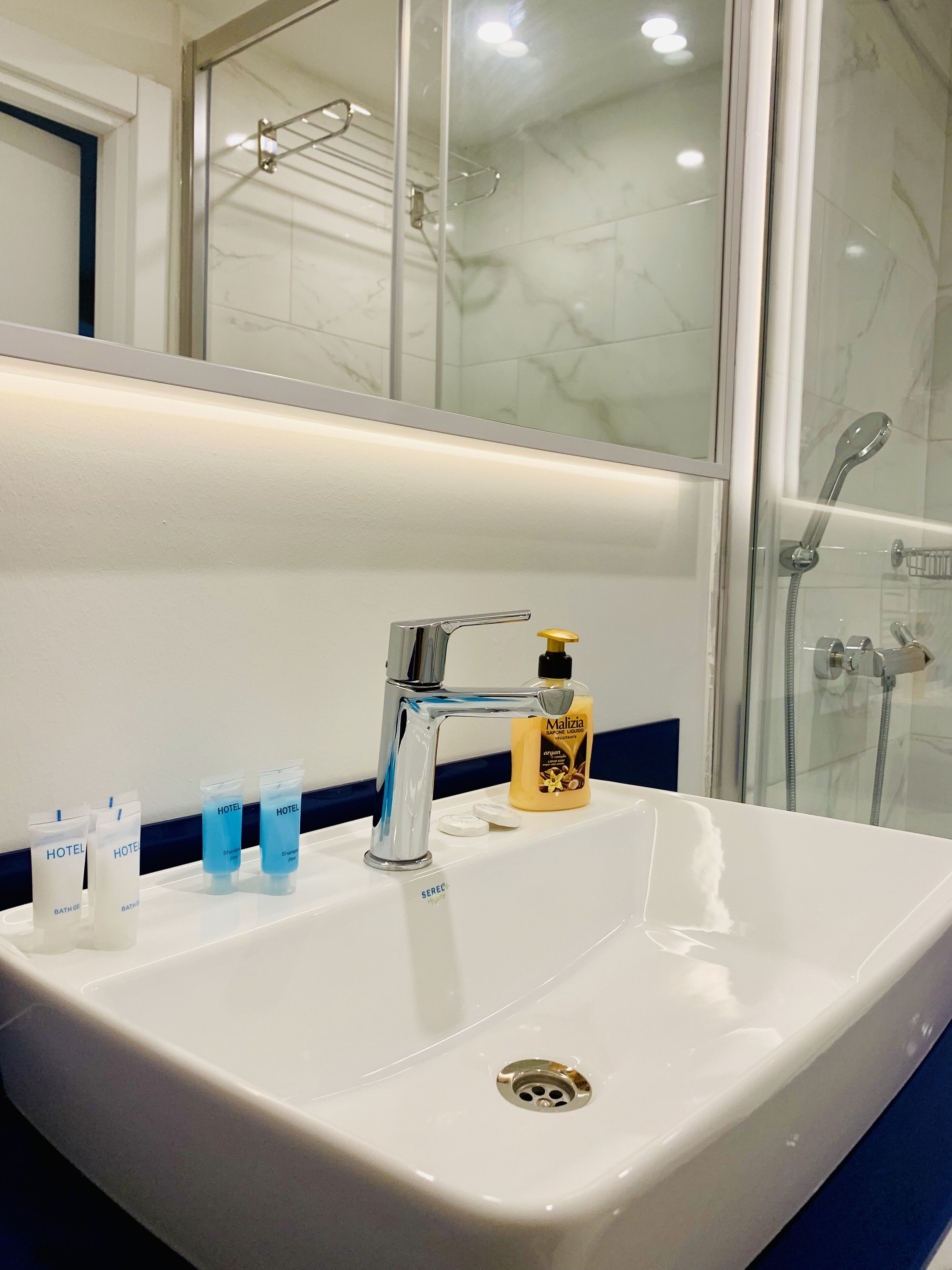 A hotel bathroom with a white sink, a mirror, and toiletries including a bottle of shampoo and soap.
