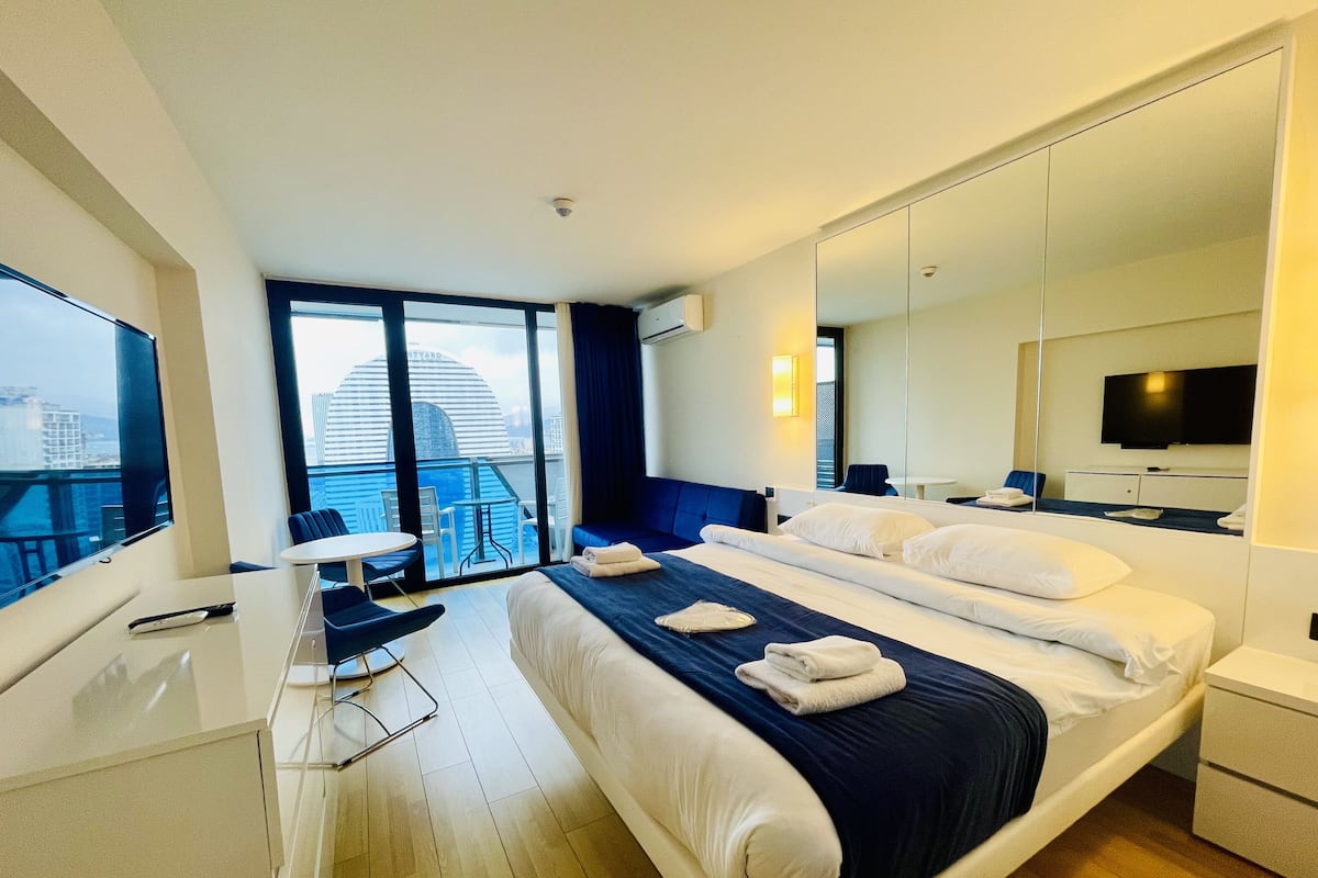 Hotelkamer met een groot bed, bureau met stoel, televisie, balkon met stadszicht en een grote spiegel.
