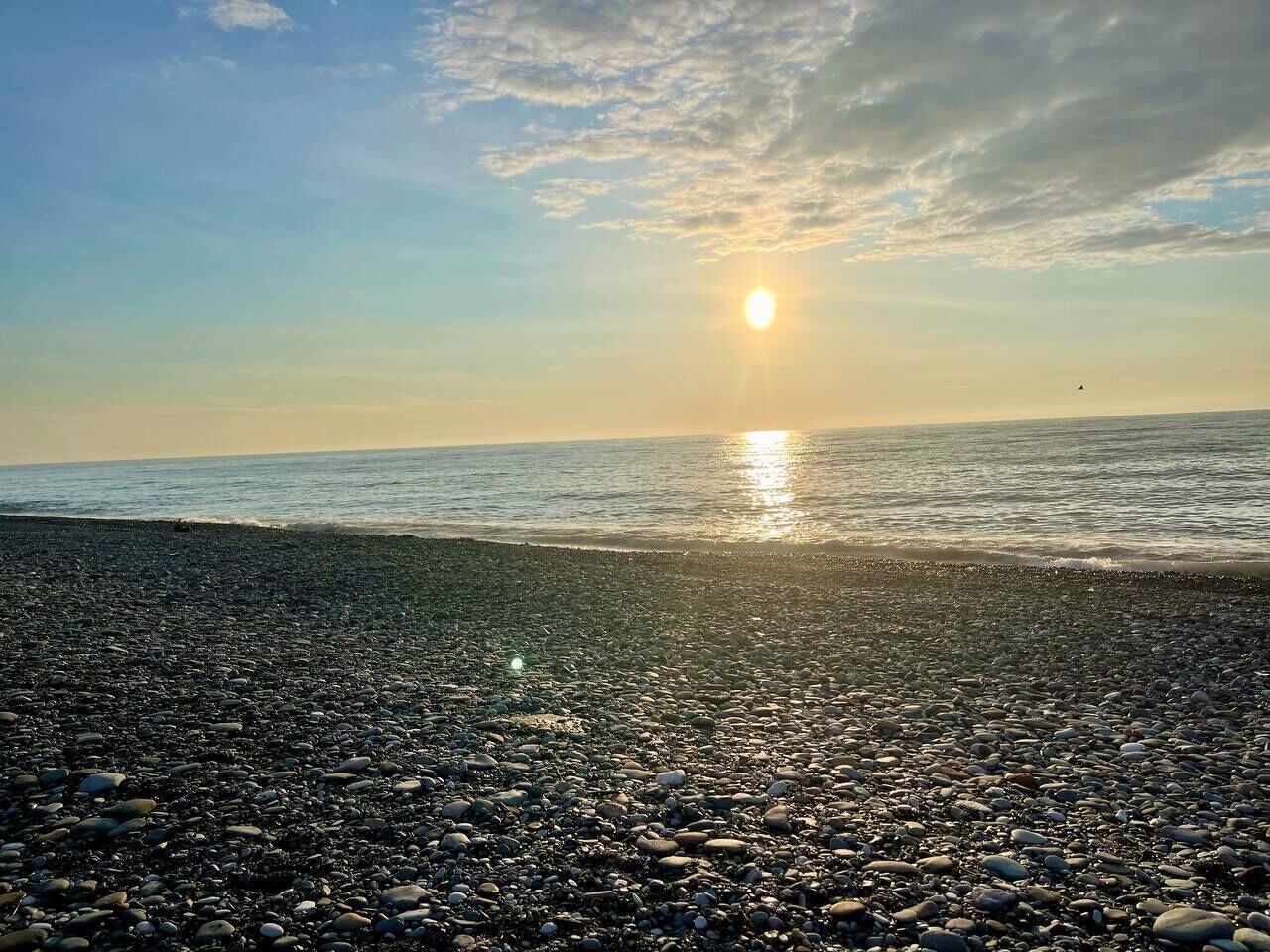 Een kiezelstrand met de ondergaande zon aan de horizon.