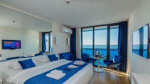 Habitación de hotel moderna con una cama grande, un escritorio con silla, televisión y vistas al mar.