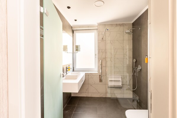 Un baño moderno con cabina de ducha de vidrio, un lavabo blanco y un inodoro.
