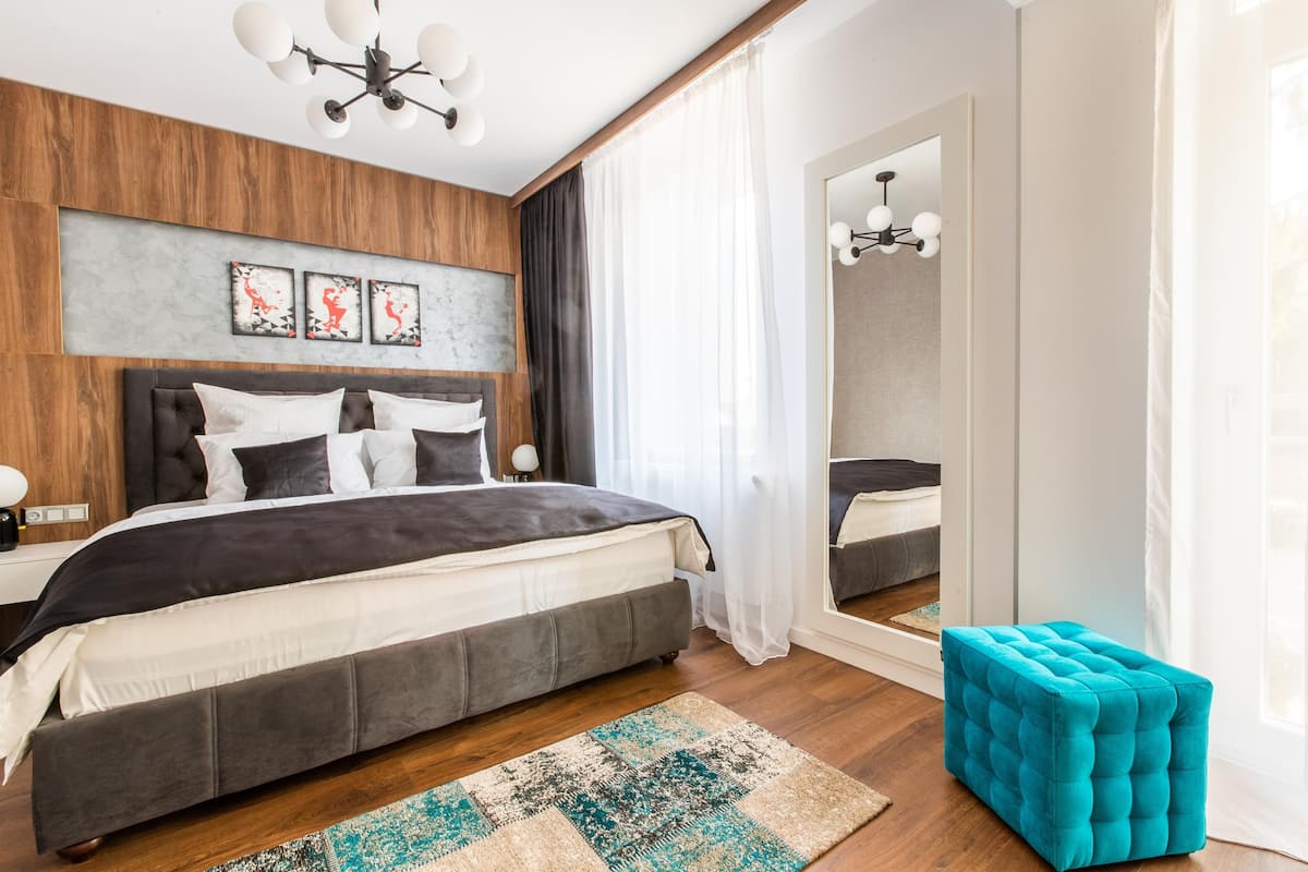 Un dormitorio moderno con una cama grande, un reposapiés capitonado, un cabecero de madera y un espejo.