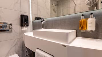 A modern bathroom with a white sink, a handheld soap dispenser, and two bottles of LAPE body wash on a gray-tiled wall.