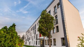 Un edificio moderno con techo plano, varias ventanas y un árbol en primer plano.