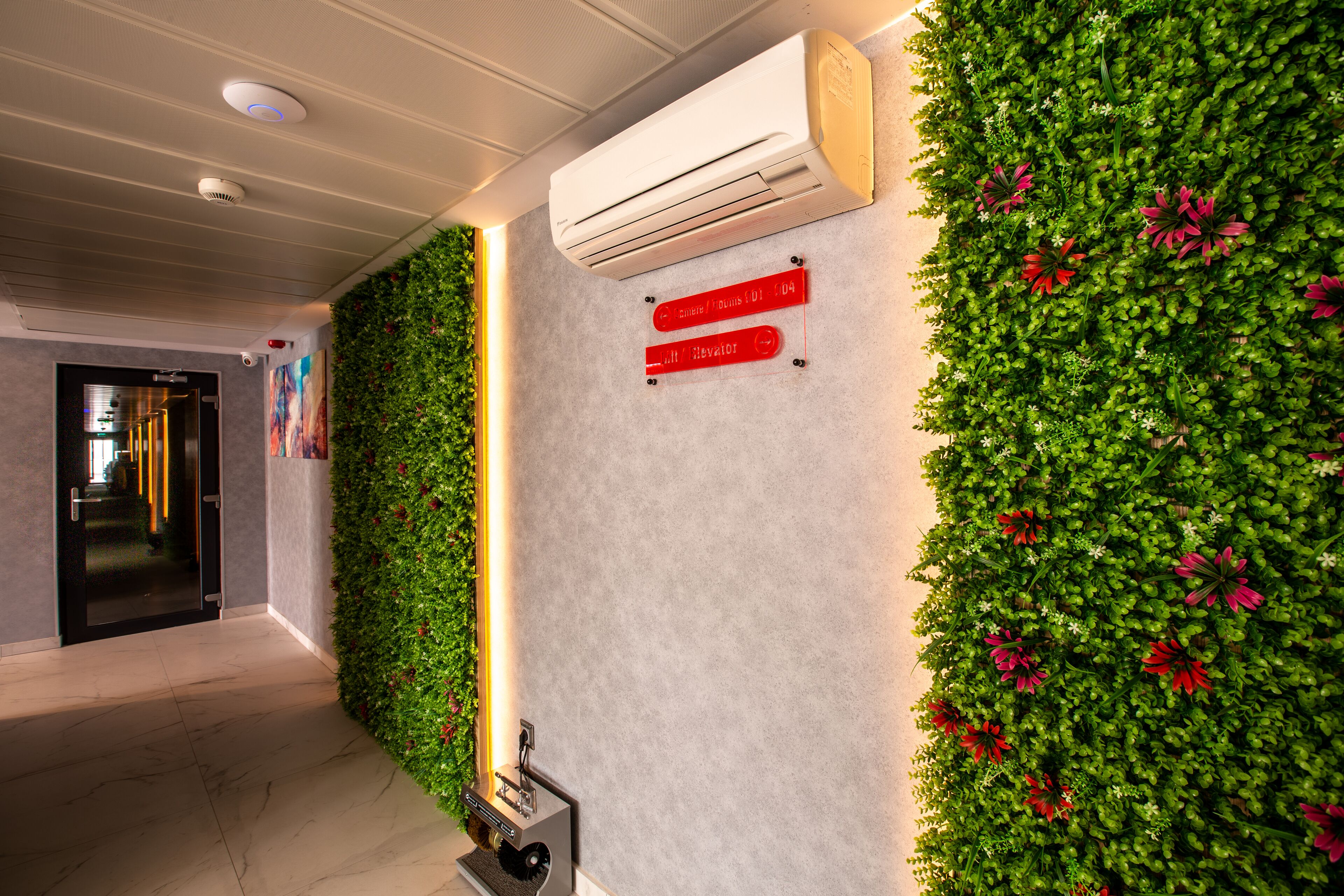Zona de recepción con pared verde, equipo de aire acondicionado y señal con instrucciones de emergencia.