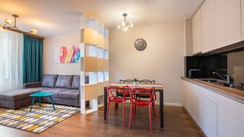 Een moderne woonruimte met een bank, een eettafel met stoelen, een keukenhoek en een trap met leuning.