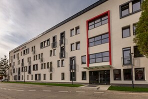 Un immeuble moderne à plusieurs étages, doté d’une façade plate, de nombreux balcons et d’un élément décoratif rouge bien visible sur le côté supérieur droit.
