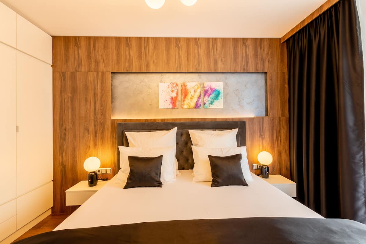 Una habitación de hotel con una cama grande, dos mesitas de noche con lámparas, un cabecero de madera y una obra de arte colgada en la pared.
