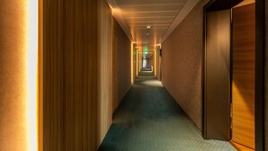 Un pasillo de hotel con alfombra estampada, paredes de madera y varias puertas que dan a habitaciones.