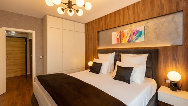 Un dormitorio moderno con una cama grande, paneles de madera, una lámpara en el techo y una obra de arte en la pared.