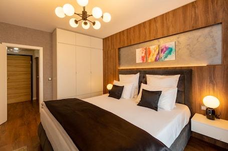 A modern bedroom with a large bed, wooden paneling, a ceiling light fixture, and a wall-mounted artwork.