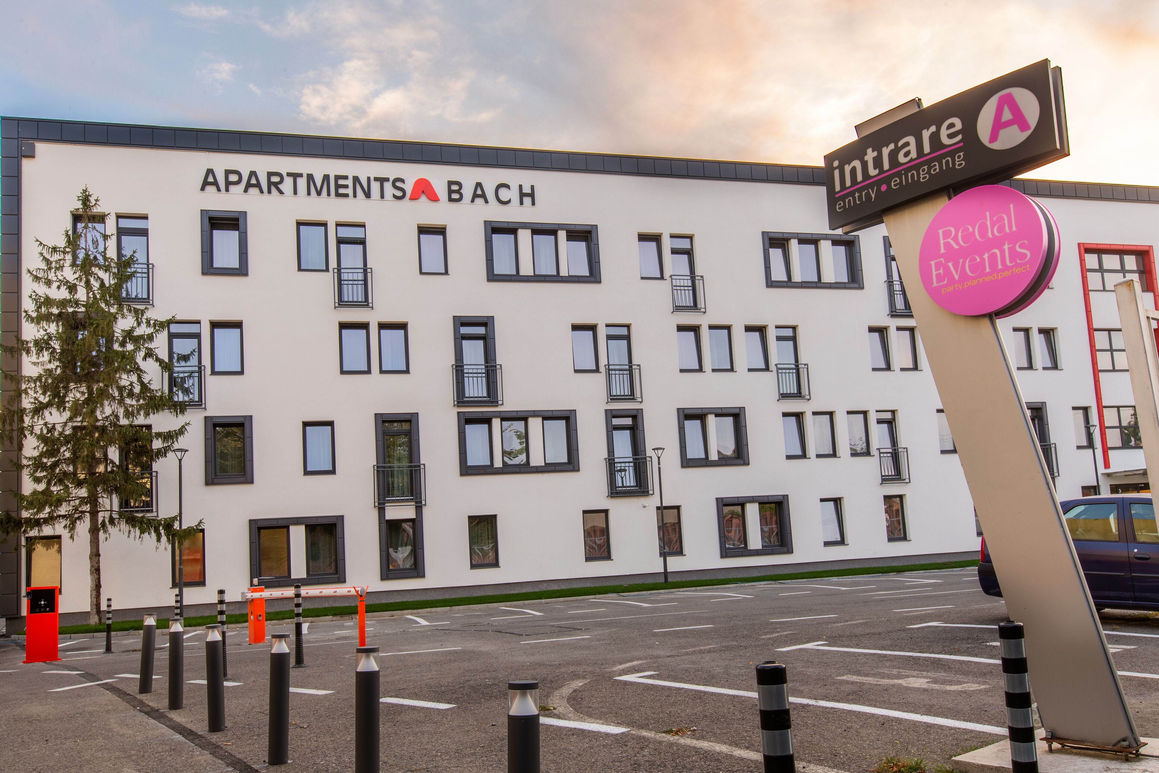 A modern apartment building with a sign indicating 'APARTMENTS A BACH' and a nearby sign for 'Redal Events'.