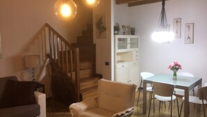 Ein gemütliches Wohnzimmer mit einer Couch, einem Sessel und einem Esstisch mit Stühlen. Eine Treppe führt auf eine höhere Ebene.